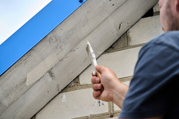 A man is painting a wall with a brush. The wall is made of bricks and the man is using a white paint