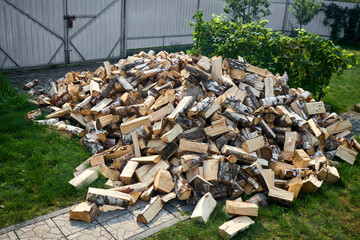 Stack of birch firewood with hand chopping block. Chopped firewood for winter. Lot of firewood - harvesting wood for heating the house. Horizontal photo. Chopped firewood on grass in yard.