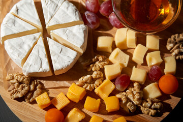 A wooden board with a variety of cheeses, nuts, and fruit. The cheeses are cut into small cubes and...