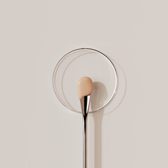Metallic spatula with test of beige liquid foundation or concealer above clear glass petri dish. 3d rendering beauty, cosmetic product, or skincare concepts with a clean aesthetic