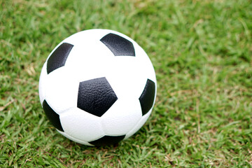 Fototapeta premium Football, with its classic black and white soccer ball placed on a green grass field, represents one of the most iconic pieces of sports equipment used in matches, training, and recreational play worl