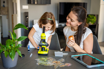 Little girl and her mother examining onion skin under a microscope at home. Concept of family...