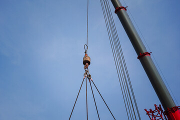 Obraz premium Crane operation during lifting a heavy object by wire rope sling equipment with blue sky background. Industrial working scene.