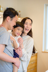 父親が子どもを抱き上げて笑顔を交わす様子を母親が見守る微笑ましい朝の風景