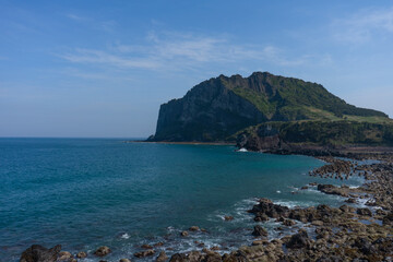 Seongsan Ilchulbong volcanic peak with tranquil mood overlooking Umutgae Coast, Jeju, South Korea, against a blue sky and ocean backdrop