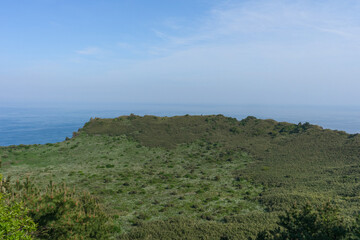 Seongsan Ilchulbong volcanic crater landscape, tranquil mood, representing Jeju, South Korea nature against a blue sky and ocean background 