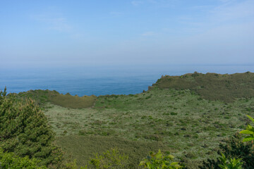 Seongsan Ilchulbong volcanic crater landscape in natural colors, Jeju, South Korea, panoramic view of coastal grassland with ocean horizon, no person