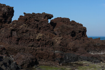 Volcanic rock formation in natural style, earthy brown and blue colors, representing Jeju South Korea Seongsan Ilchulbong coastline