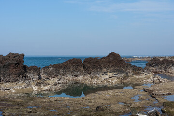 Volcanic rock coastline landscape, natural light, Jeju, South Korea, Seongsan Ilchulbong, blue sky, tranquil ocean view, no person
