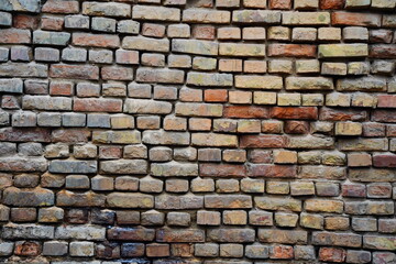 A large wall made of old bricks with dents, cracks and irregularities.