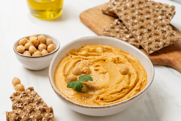 reamy hummus in a white bowl, garnished with chickpeas and herbs, paired with crispy flatbreads and olive oil, showcasing a vibrant and appetizing snack presentation