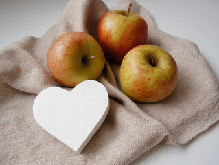 Fresh red apples with white wooden heart on beige cloth napkin, minimalist kitchen decor for healthy eating, Valentine's gifts, rustic home styling with natural light and organic textures. 