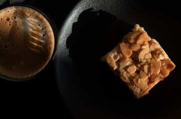Tarta de almendra con café con leche con fondo oscuro.