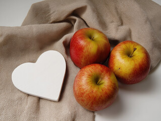 Fresh red apples with white wooden heart on beige cloth napkin, minimalist kitchen decor for healthy eating, Valentine's gifts, rustic home styling with natural light and organic textures. 