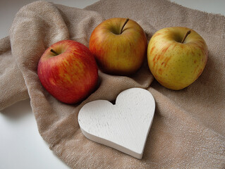 Fresh red apples with white wooden heart on beige cloth napkin, minimalist kitchen decor for healthy eating, Valentine's gifts, rustic home styling with natural light and organic textures. 