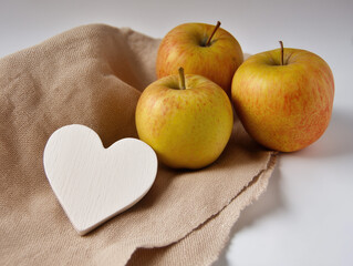 Fresh red apples with white wooden heart on beige cloth napkin, minimalist kitchen decor for healthy eating, Valentine's gifts, rustic home styling with natural light and organic textures. 