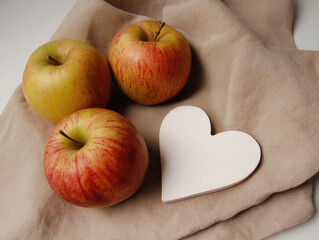 Fresh red apples with white wooden heart on beige cloth napkin, minimalist kitchen decor for healthy eating, Valentine's gifts, rustic home styling with natural light and organic textures. 