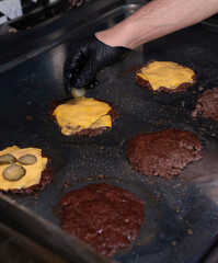 Chef adding cheddar cheese and pickles on smash burgers during preparation..