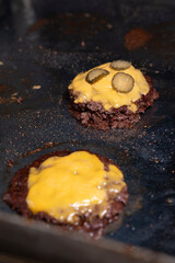 Chef adding cheddar cheese and pickles on smash burgers during preparation..