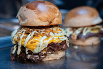 Freshly made double smash burgers with melted cheddar, grilled onions, and sauce on a shiny countertop..