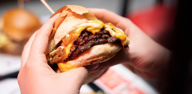Hands holding a juicy double smash burger with melted cheddar and onions..