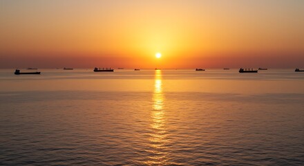 Obraz premium Cargo ships silhouetted against a warm golden sunset over a calm ocean