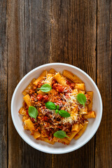 Rigatoni con ragù alla bolognese - noodles with bolognese sauce and grated parmesan cheese served in bowl on wooden table	
