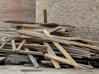 Multiple wooden planks are piled up carelessly beside a brick wall in a construction site,...