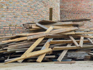 Piled wooden planks rest against a brick wall, showing signs of use at a construction site during...