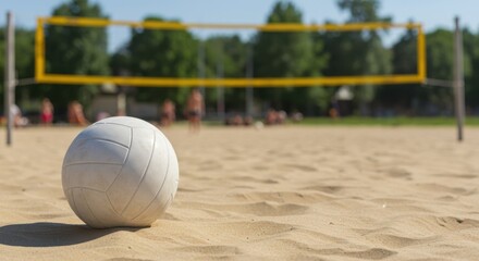 A volleyball resting on sand near a net with trees and people in the blurred background outdoors