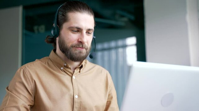 Corporate operator in headset working in customer support service on helpline telesale talking using laptop in business office. Agent of call center advises the client by answering questions. Close up