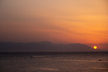 Obraz premium A vibrant sunset over the sea in Loutraki, Greece. Warm golden and pink tones fill the sky above the calm water, creating a romantic and tranquil moment.