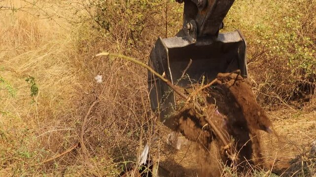 JCB crane working near sand quarry outdoors in the nature during summer season. Excavator arm is digging the sand on a modern construction site. JCB is extracting sand from a vast sand field.