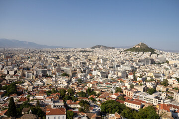 Obraz premium A panoramic view of Athens, Greece, seen from above. The city stretches out with a mix of historic and modern buildings, surrounded by hills under an open sky.