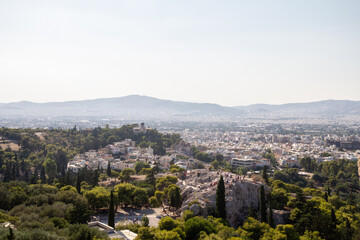 Obraz premium A panoramic view of Athens, Greece, seen from above. The city stretches out with a mix of historic and modern buildings, surrounded by hills under an open sky.