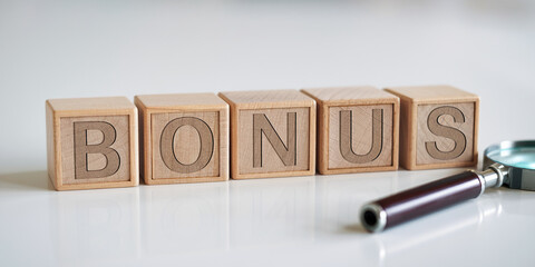 Wooden blocks spelling BONUS, next to magnifying glass on white background, showcasing business concept, reward, or incentive
