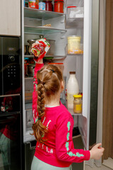 little girl taking food out of fridge at home in kitchen