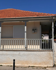 Exterior of a classic house with red tiled roof, closed white shutters, and railing, under clear blue sky, captured in natural daylight