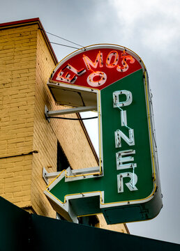 Durham, NC - US - May 4, 2025 Vintage neon sign for Elmo's Diner glows against a cloudy sky, mounted on a yellow brick building with a bold green arrow pointing toward classic comfort food.