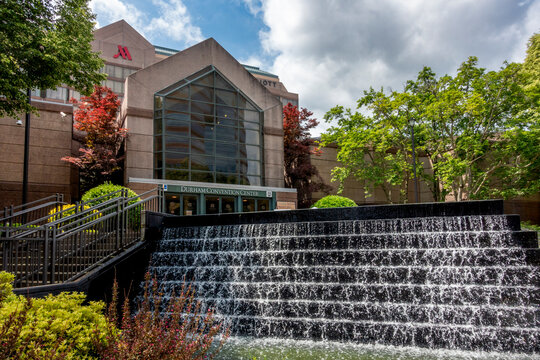 Durham, NC - US - May 3, 2025 The Durham Convention Center stands behind a cascading black stone fountain, framed by lush greenery and a modern glass entrance beneath the adjoining Marriott