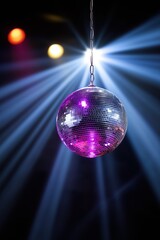 A disco ball is suspended from a chain and is illuminated by a bright light. The ball is purple and silver, and it is surrounded by a blue light. The scene is set in a club or party setting