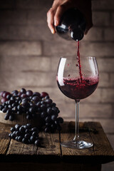 Pouring red wine into the glass against wooden background