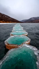 Fototapeten Frozen Shoreline with Teal Ice Circles and Mountain Background © sukahati