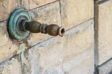 Close up of old retro metal water faucet on old stone countryside fountain with running water
