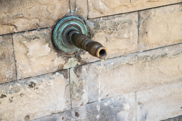 Close up of old retro metal water faucet on old stone countryside fountain with running water