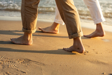 Close-up of couple's bare feet walking on sandy beach at sunset. Lifestyle. Vacations.