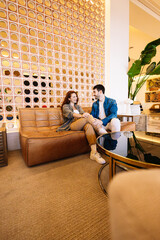 Couple chatting on stylish leather sofa in modern hotel lobby. Lifestyle.