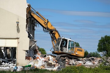 A yellow crane demolishing an old house