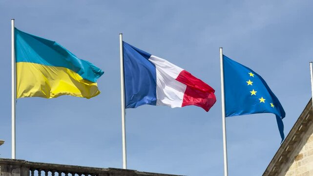 Flags of Ukraine, France, and the European Union waving in the wind against a blue sky, symbolizing unity, diplomacy, and international cooperation.