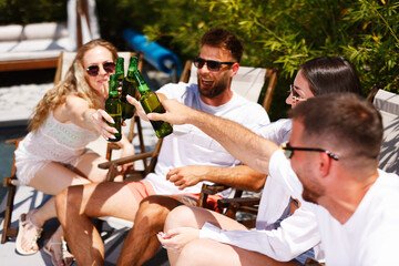 Friends toasting with beer bottles at a pool party